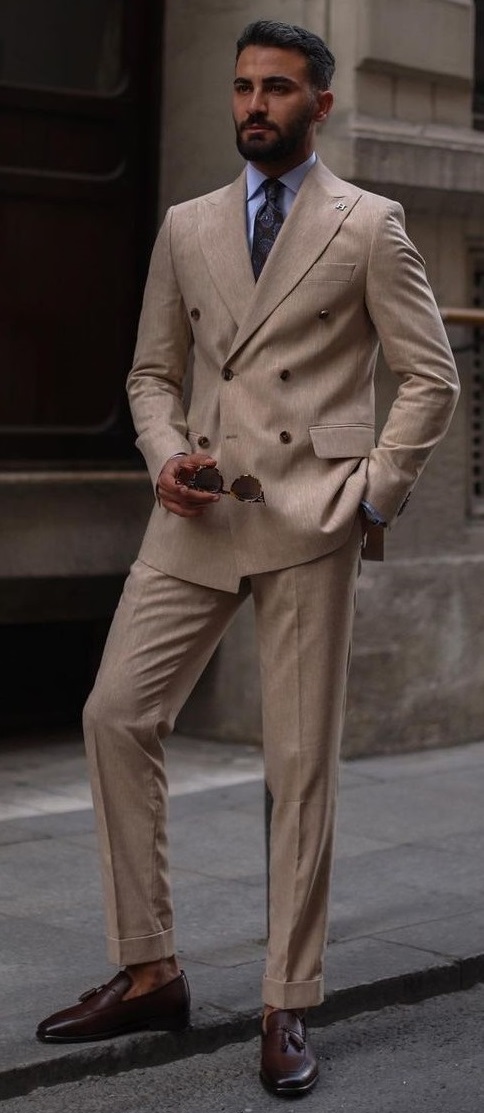 double breasted beige suit with blue shirt and a printed tie, holding shades in hand_ double breasted beige suit with blue shirt and a printed tie, holding shades in hand_