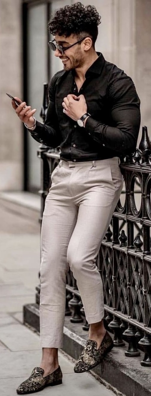 black shirt accessorized with suedes, watch and shades, happily standing with a mobile black shirt accessorized with suedes, watch and shades, happily standing with a mobile
