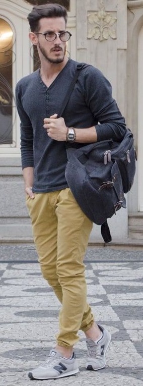 beige chino joggers with grey full-sleeved tshirt and shades, accessorized with glasses and watch holding a bag in shoulders beige chino joggers with grey full-sleeved tshirt and shades, accessorized with glasses and watch holding a bag in shoulders