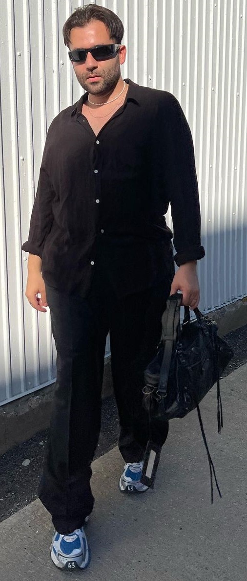 Balenciaga City Bag with black chinos and black shirt, accessorized with shades and completing the look with sneakers, being one of the must-have products to own