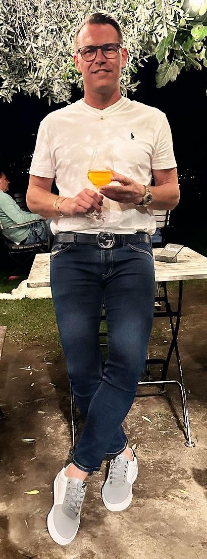 a blue denim with a white tshirt, accessorized with a Gucci belt being a must-have product to own with glasses and a watch and a glass of drink a blue denim with a white tshirt, accessorized with a Gucci belt being a must-have product to own with glasses and a watch and a glass of drink